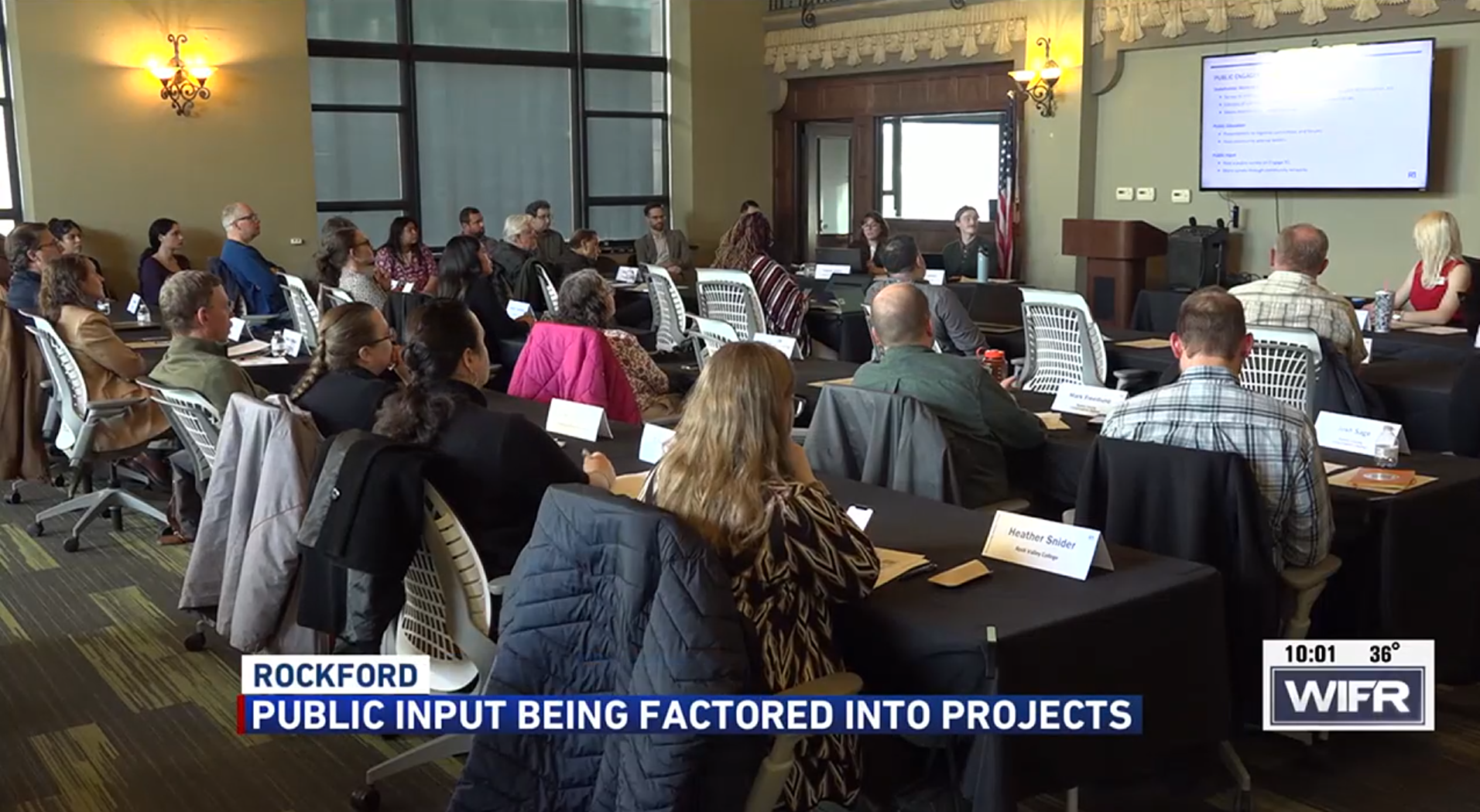 News Cast Image of the Community Advisory Forum meeting of many people looking at a tv