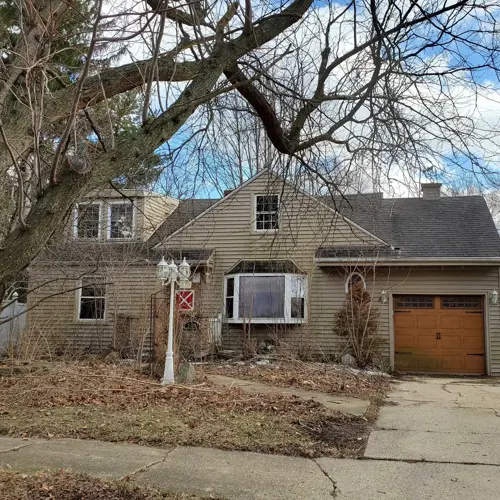 tan two-story house from front. Attached garage to right side with wooden door.