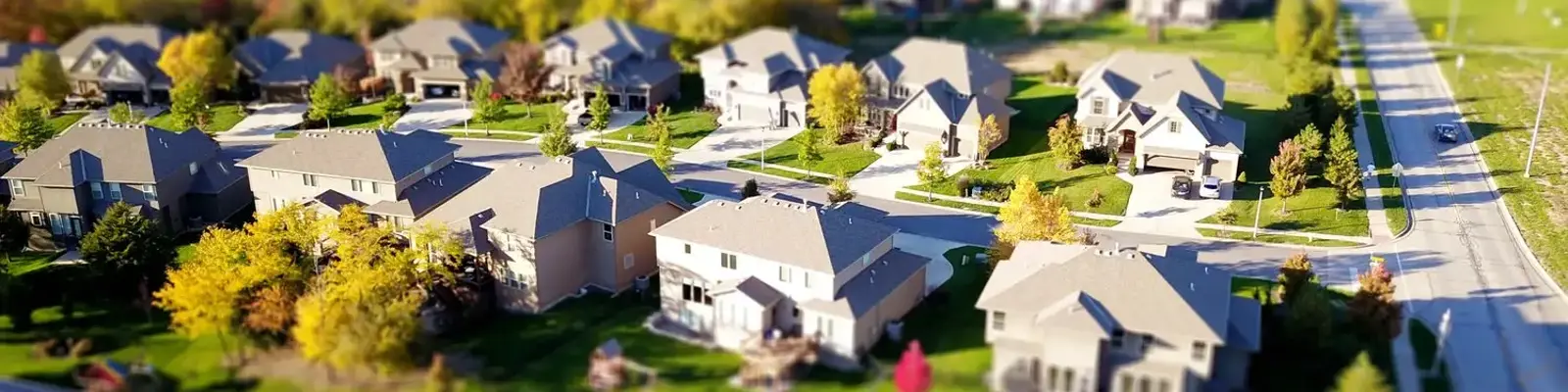 Neighborhood with rows of white two-story houses in a subdivision. Main road to the right of image and agricultural field on other side of the road.