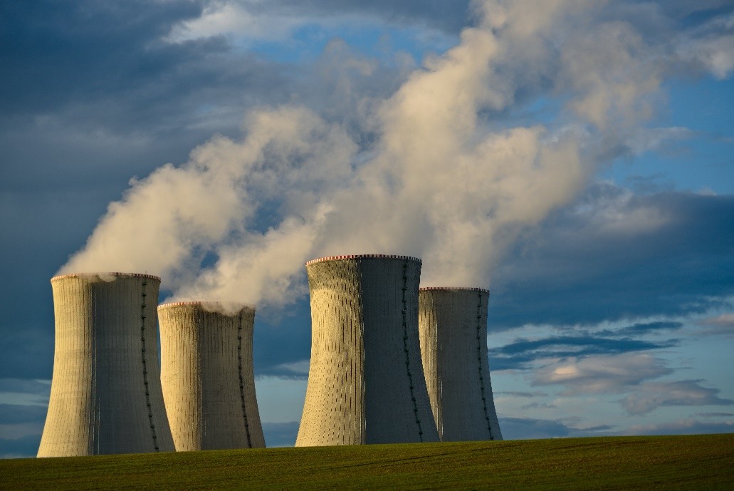Alt Text: 4 gray nuclear plant cooling towers emitting water vapor in a field 